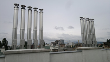 Several tall metal exhaust stacks rise from a rooftop under a cloudy sky.