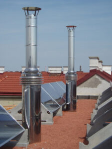 Rooftop features tall metallic vent pipes and rows of solar panels on red roof tiles under a blue sky.