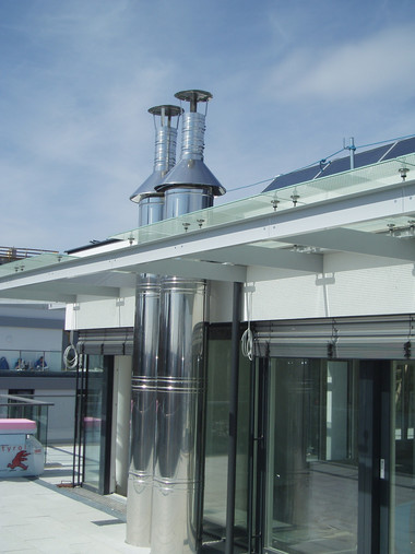 Rooftop terrace with shiny stainless steel vent stacks and glass doors under a clear blue sky.