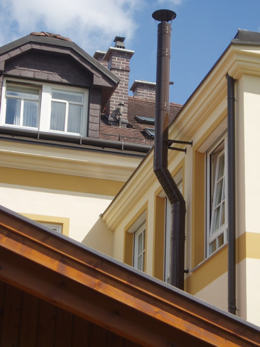 Yellow building with white-trimmed windows, a dark vertical downspout, and a brick chimney against a blue sky.