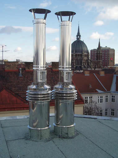 Two tall shiny metal vent pipes on a rooftop with a city skyline and a domed building in the background.