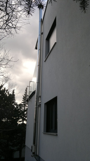 Side view of a white multi-story apartment building with balconies, framed by trees and a cloudy sky.