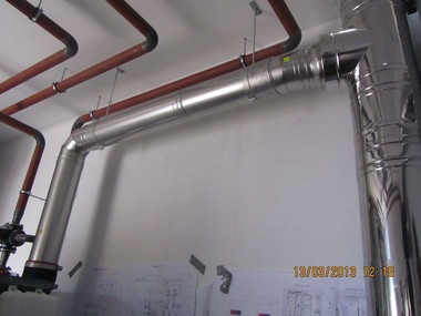 Silver insulated pipes and copper tubes run along a gray wall in a mechanical room.