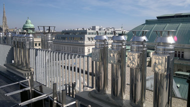 Ornate metal railing on a rooftop overlooks a city skyline with domed and green-roofed buildings.