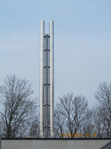 Tall metal radio antenna tower rises above a flat rooftop with leafless trees in the background.