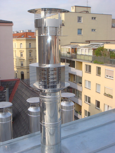 Shiny metal ventilation pipes rise from a rooftop, with apartment buildings in the background.