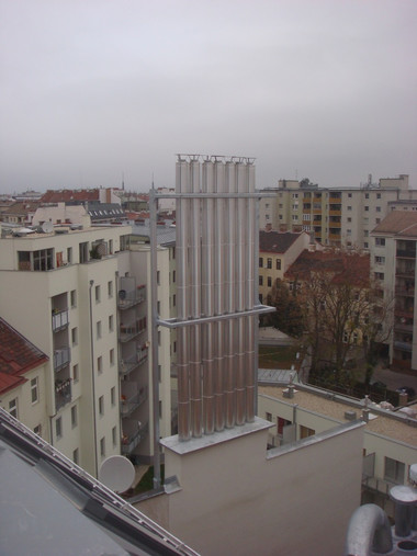 Overcast cityscape with a tall rectangular metal antenna on a rooftop among surrounding apartment buildings.