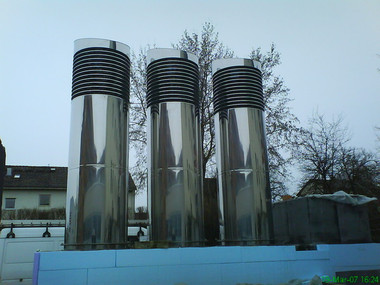 Three tall stainless steel vent pipes with black ribbed caps on a blue platform outdoors.
