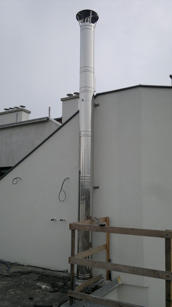 Tall metal vent stack rises from a flat roof beside a white building.