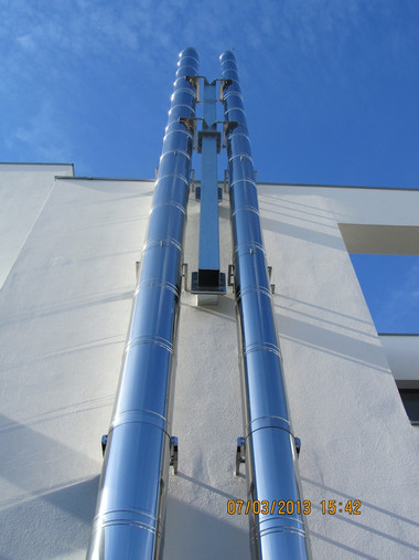 Two parallel shiny metal ducts run vertically along the white building against a bright blue sky.