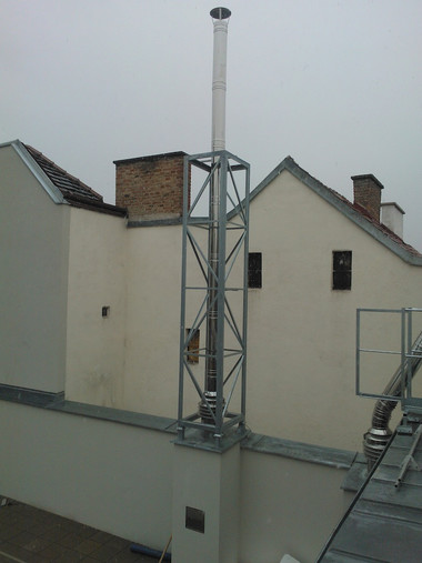 Tall metal lattice antenna on a flat rooftop with beige buildings in the background.