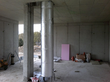Interior of a partially completed building with concrete columns, exposed walls, and scattered construction materials on the floor.
