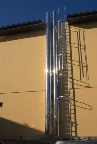 Beige building exterior with two tall chrome pipes and a metal ladder attached to the wall.