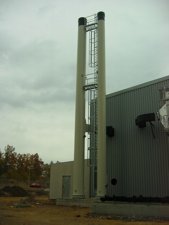 Tall metal tower with a ladder beside a corrugated metal building in an industrial area.