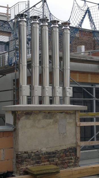 Six tall porcelain insulators mounted on a concrete pedestal on a rooftop, with scaffolding and safety netting in the background.