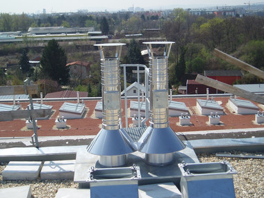 Two blue cone-shaped roof vents with tall metal chimneys on a flat rooftop, with other equipment and trees in the background.