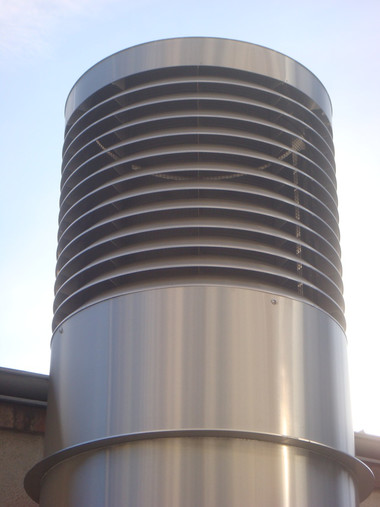 A tall metal vent stack with many horizontal slats against a clear blue sky.