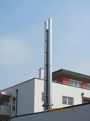 Tall metal vent stack rises from a white building roof against a blue sky.