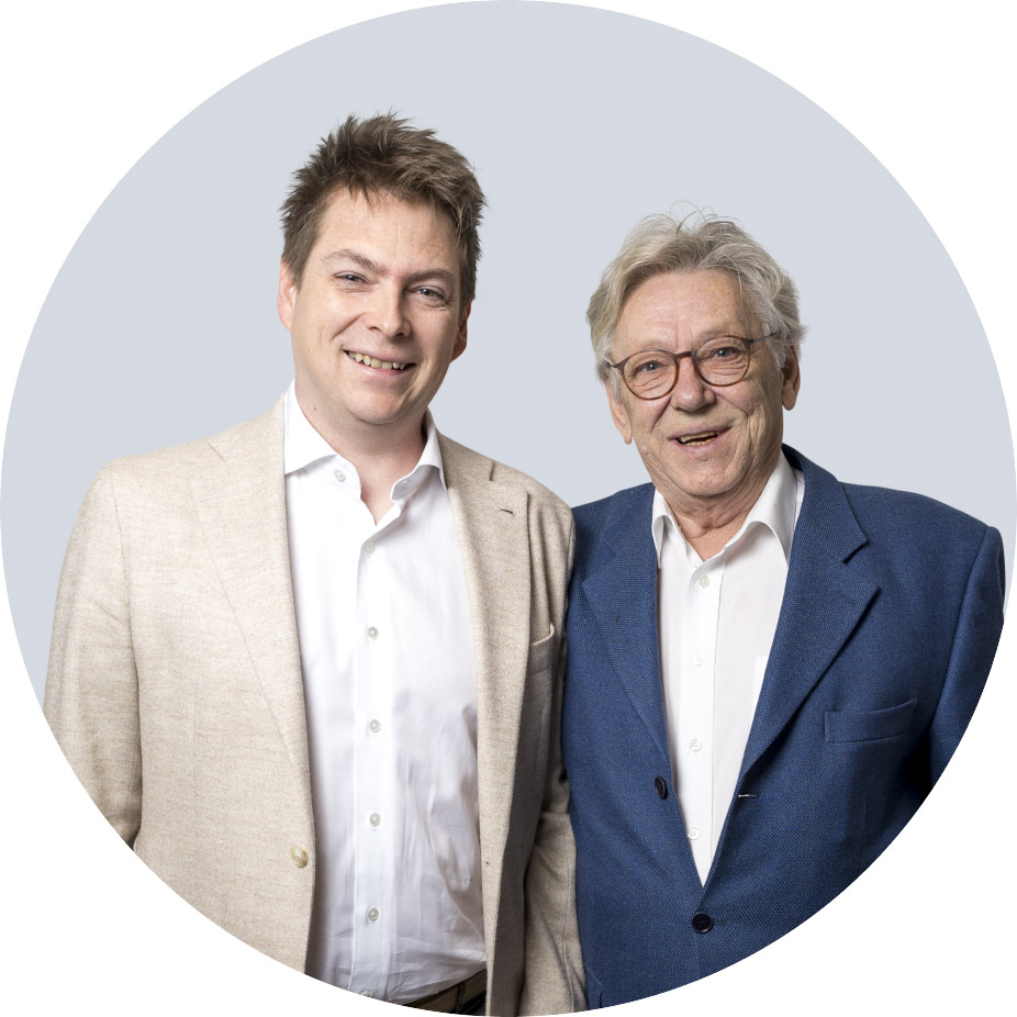 moldrich-26-unternehmen-01 Two smiling men in business attire stand side by side against a pale blue circular background.