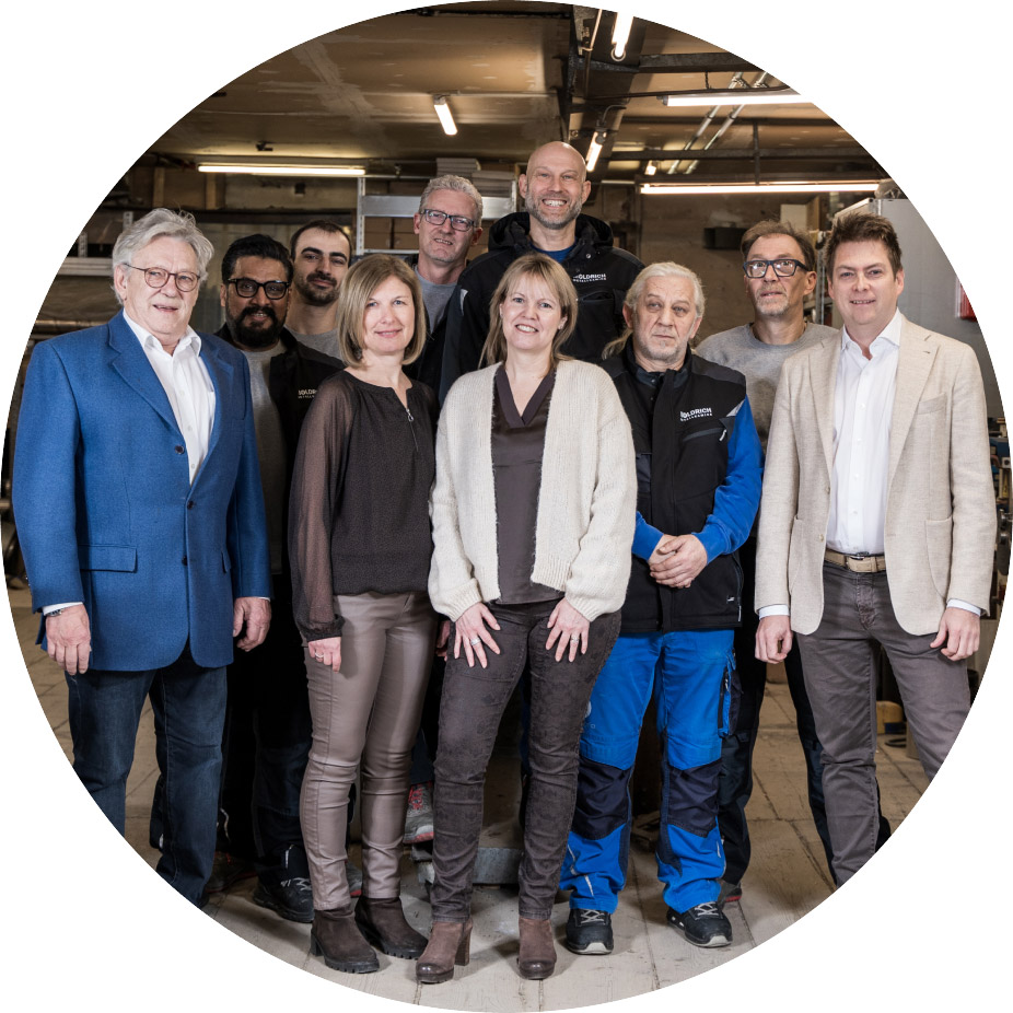 moldrich-26-unternehmen-02 A diverse group of colleagues posing together in an industrial workshop setting.
